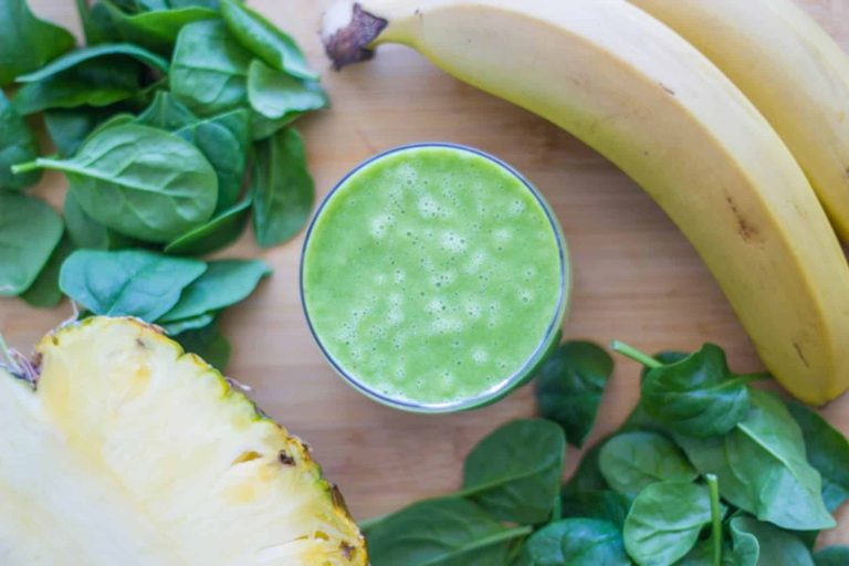 A refreshing glass of spinach pineapple banana smoothie with a creamy texture, garnished with a pineapple slice and chia seeds, placed on a wooden table.