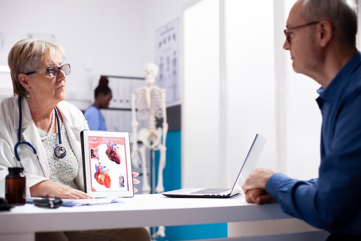 Doctor showing patient a heart anatomy diagram on a tablet while explaining coronary thrombosis vs myocardial infarction during a cardiology consultation.
